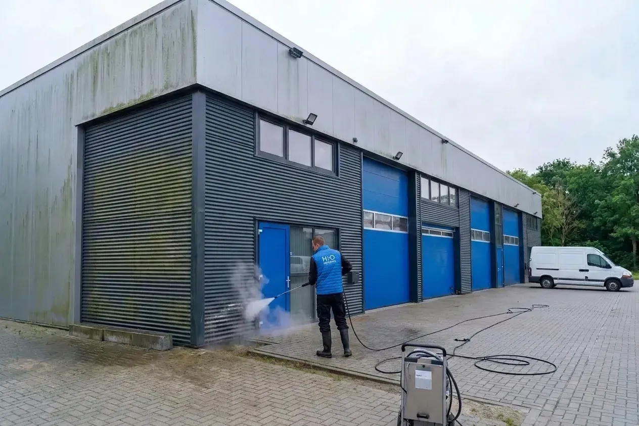 Professional commercial building cleaning service removing moss and algae from corrugated metal cladding on an industrial building exterior